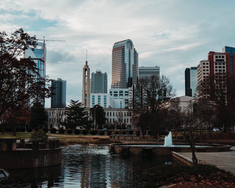 city view of charlotte nc by pond with fountain - photo by Pexels