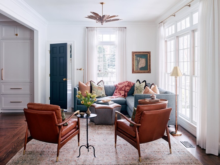 Sitting area adjacent to the kitchen in a Charlotte, NC remodel featuring leather lounge chairs, a blue sectional sofa, oversized windows, layered neutral textiles, and a navy accent door in a bright transitional interior. Sitting area adjacent to the kitchen in a Charlotte, NC remodel featuring leather lounge chairs, a blue sectional sofa, oversized windows, layered neutral textiles, and a navy accent door in a bright transitional interior.