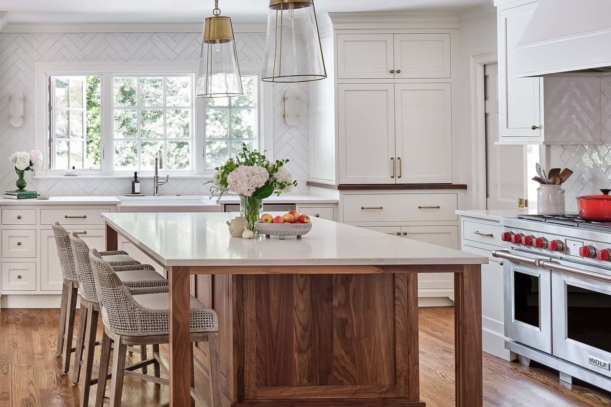 Bright white kitchen remodel in Charlotte, NC with a walnut island, Sereno Gold quartz countertops, brass and glass pendant lighting, white shaker cabinetry, Wolf dual-fuel range, and warm hardwood floors by Hopedale Builders